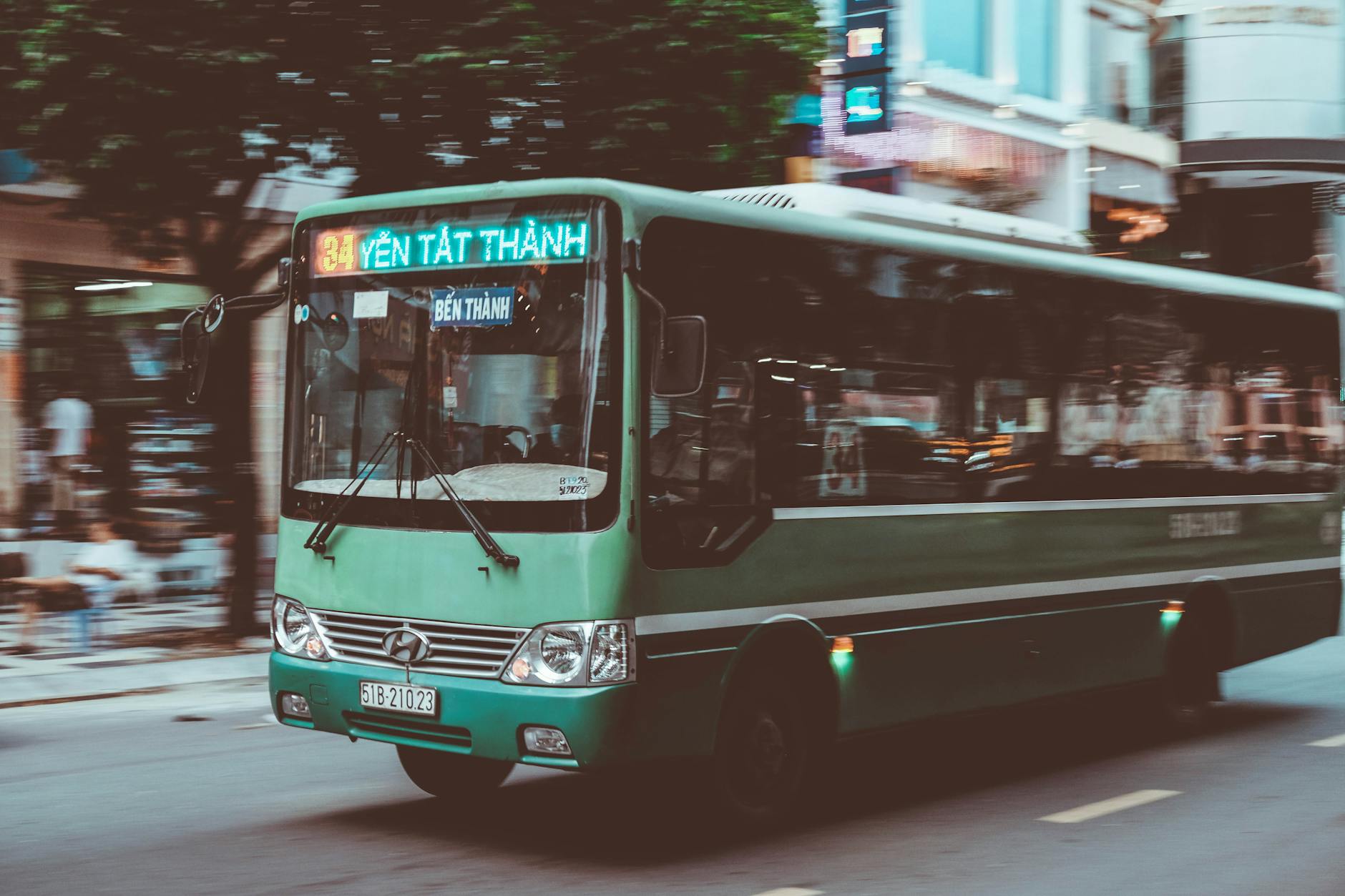 Green Hyundai bus on a bustling urban street in Vietnam, showcasing city life.
